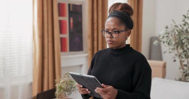 Gülümseyen çekici kız, taşındıktan sonra evi dekore etmek için internetten mobilya sipariş ediyor. Evinde nasıl görüneceğini değerlendiriyor. Tablet kullanıyor.