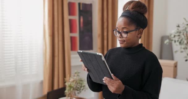 Ein junges Mädchen bestellt Möbel für neue Wohnung online schmückt Haus nach dem Einzug sucht nach Dekoration Inspiration schaut sich in ihrem Zimmer mit Tablet um — Stockvideo