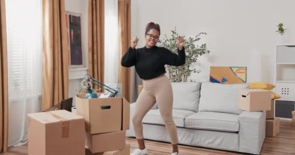 Счастливая женщина, танцующая посреди комнаты, хлопая в ладоши, качаясь в ритме музыкальной радости от переезда в арендованные картонные коробки с упакованными вещами — стоковое видео