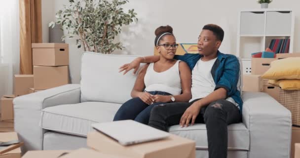 Małżeństwo siedzi na kanapie po przeprowadzce przytulić się plan relaksu renowacja mieszkania kupili spin wizje omówić — Wideo stockowe