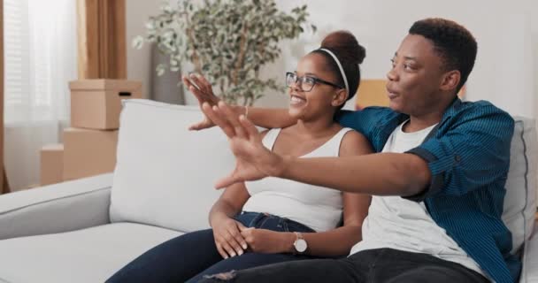 Um casal se senta no sofá depois de se mudar abraçar uns aos outros relaxar planejar a renovação do apartamento que eles compraram visões spin discutir — Vídeo de Stock