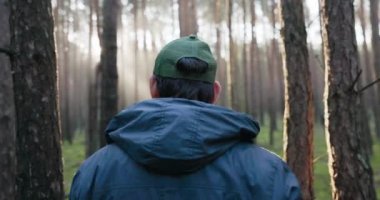 Bir adam gün doğumunda ormanda yürür, ağaçların dallarını yaran ışınlar, doğanın içinde sabah, yosun, yaprak parıltısı, ağaçların büyülü manzarası, sis, ağızdan buhar.