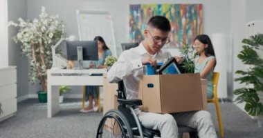 Gözlüklü, yaralı, sakat, tekerlekli sandalyeli genç bir ofis çalışanı kucağında bir kutu alet edevat tutuyor, emekli oluyor, işten çıkarılıyor, işsiz kalıyor, pozisyon değiştiriyor.