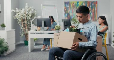 Gömlek giymiş engelli bir adam şirket ofisinde işe girdi. Tekerlekli sandalyede oturuyor. İçinde iş eşyalarıyla birlikte.