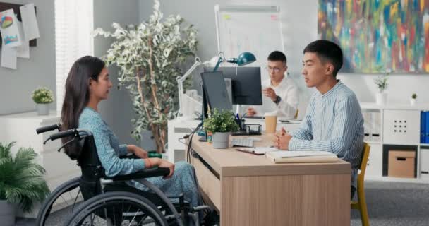 La mujer está sentada en silla de ruedas en el escritorio de la oficina, frente a su empleador se extiende la mano, se estrechan las manos agradeciéndose mutuamente por la entrevista felicitando el saludo diciendo adiós — Vídeos de Stock