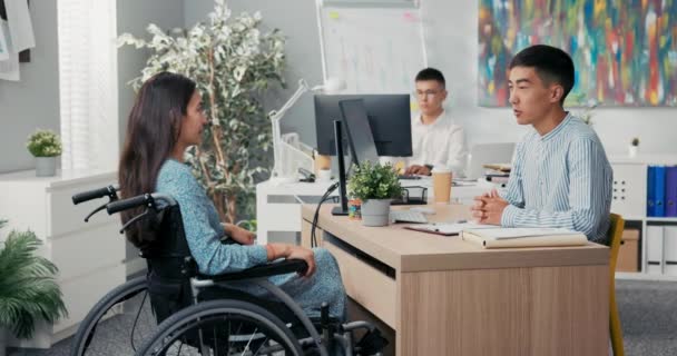 La mujer está sentada en silla de ruedas en el escritorio de la oficina, frente a su empleador se extiende la mano, se estrechan las manos agradeciéndose mutuamente por la entrevista felicitando el saludo diciendo adiós — Vídeos de Stock