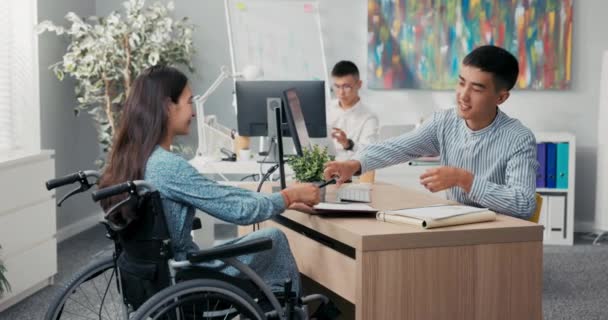 La mujer está sentada en silla de ruedas en el escritorio en la oficina a través del empleador que están firmando el hombre contrato empleado extiende la mano, se dan la mano agradeciéndose mutuamente por la conversación felicitando — Vídeo de stock