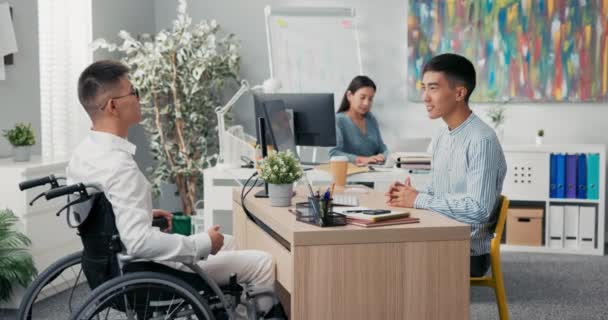 Intervista di lavoro con l'uomo disabile in sedia a rotelle dopo un incidente, infortunio, capo elegantemente vestito seduto alla scrivania sorride al candidato, fargli domande, futuro dipendente racconta di esperienza — Video Stock