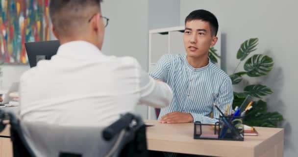 Zwei Männer treffen sich morgens im Firmenbüro zum Vorstellungsgespräch behinderter Junge kommt im Rollstuhl mit weißem Hemd Chef sitzt ihm gegenüber schüttelt Hände, um ihn zum Abschied zu begrüßen gratulieren — Stockvideo