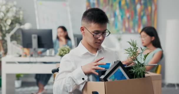 Sonriente, hombre alegre en gafas es discapacitado monta silla de ruedas por esta razón obtiene una promoción a otra posición, sostiene en el regazo una caja de cartón con cosas, accesorios, comprueba la integridad — Vídeos de Stock