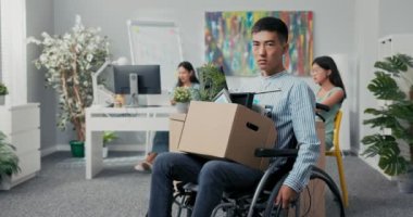 Asyalı güzel gömlekli hırslı bir adam tekerlekli sandalyede, dizlerinin üzerinde karton kutuyla şirkette oturuyor, işinden kovuluyor ve görevini yerine getiremiyor.