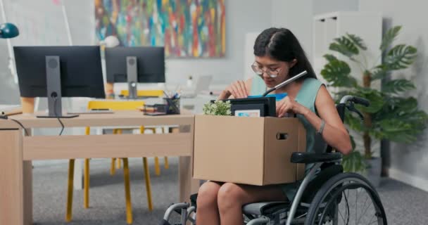 Χαμογελώντας νεαρές γυναίκες με γυαλιά είναι ανάπηρη είναι σε αναπηρική καρέκλα και εξαιτίας αυτού προήχθη σε άλλη θέση, κρατά ένα χαρτόκουτο με πράγματα στην αγκαλιά που κοιτάζει μέσα — Αρχείο Βίντεο