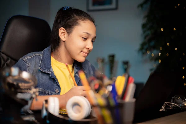 Kız dizüstü bilgisayarın önünde özenle çalışıyor, defterinde kalem olan notlar, yeniden yazıyor, e-kitap okuyor, uzaktan eğitim alıyor, sınava hazırlanıyor, uzaktan ders veriyor.