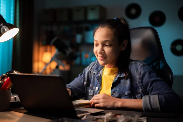 Орієнтований усміхнений підліток використовує ноутбук вдома, дивлячись на екран, балачки, читання або написання електронної пошти, папір для школи Ліцензійні Стокові Фото