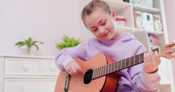 Adolescente chica está jugando la guitarra sentado en la silla delante de la computadora. — Vídeos de Stock