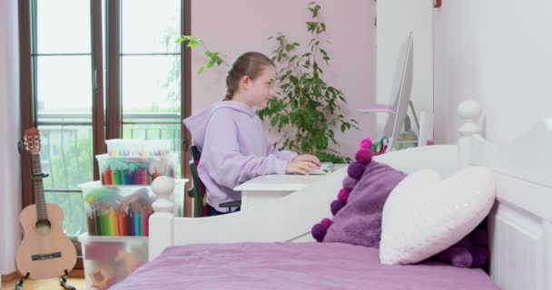 Teen girl typing on keybord and scrolling mouse, working with computer, μπροστά από την οθόνη, στο δωμάτιό της, με κρεβάτι στο πρώτο σχέδιο, πράσινα φυτά σε βιολετί φόντο, και κιθάρα πίσω της Ξαφνικά — Αρχείο Βίντεο