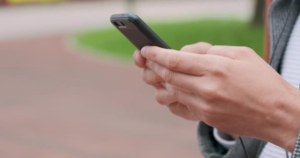 Close up of young mans hands who is leaning his back against the pole, typing a message in smartphone Camera is moving left to right — Stock Video