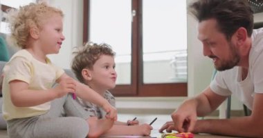 Küçük bir oğlanla küçük bir kızın yakınından geçerken, babaları yerdeki beyaz kağıda kalemle resim çiziyor birbirlerine bakıyor, kalemlere, kâğıtlara, çocuklara makaslara ve kağıt bıçaklara gülüyor.