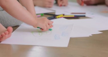 Arka planda bulanık elleri olan, ağabeyi ve babasıyla birlikte, yerdeki beyaz kağıda kalemle çizen küçük bir kızın ellerini kapatın.