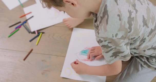 白い紙の上に鉛筆で絵を描いている小さな男の子と女の子の手と足の終わり鉛筆と紙はそれらの前にあります — ストック動画