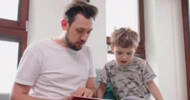 Baba ve oğulun yakın çekimleri kanepede kitap okuyarak ve resimlerden bir hikaye yazarak evde vakit geçiriyorlar.