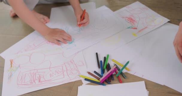 Közelkép egy kislányról és egy kisfiúról, és az apjuk hajnaláról, és a kezükről A család ceruzával rajzol a fehér papírra a padlón Ceruzák, papír van előttük. — Stock videók