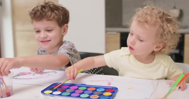Bruder und Schwester malen Aquarelle, während sie am Tisch sitzen Mädchen versucht, Pinsel in Aquarelle zu tauchen — Stockvideo