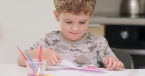 Närbild av en liten pojkar, som bara klippa och rita ett rött hjärta med akvareller och presentera den för kameran, leende — Stockvideo