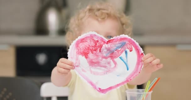 Close up de um coração vermelho, cortado e desenhado pela menina com aquarelas Apresentando-o à câmera, ela está cobrindo seu rosto — Vídeo de Stock