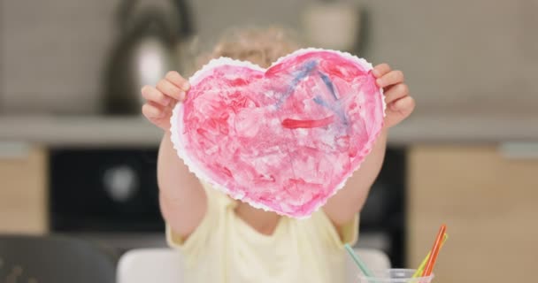 Primer plano de un corazón rojo, cortado y dibujado por la niña con acuarelas Presentándolo a la cámara, se cubre la cara — Vídeos de Stock