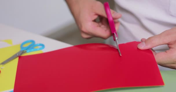 Zamknij męskie dłonie, podczas gdy on wycina nożyczkami przedmiot z kolorowego papieru — Wideo stockowe