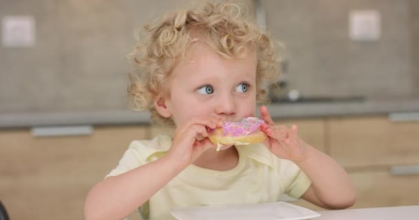 Sevimli küçük kız mutfak masasında otururken donut yiyor. — Stok video