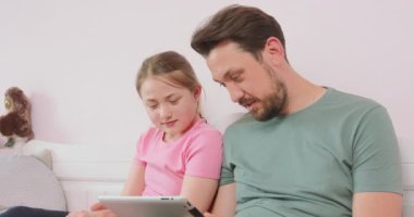 Baba ve genç kız kanepede oturup tabletteki fotoğraf albümüne bakıyorlar.