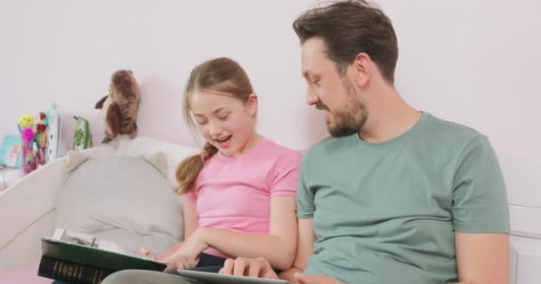 Father and teen daughter are sitting on the sofa, and are looking at the photo album - they are particularly interested in one photo — Stock Video