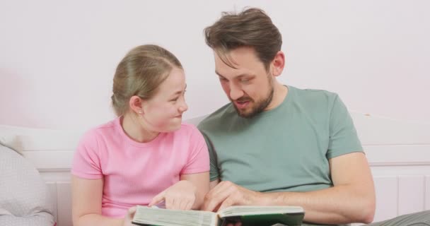 Father and teen daughter are sitting on the sofa, and are looking at the photo album The girl laughs and wipes the eye — Stock Video