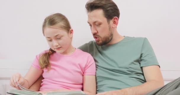 Close up of father and laughing teen daughter sitting on the sofa, and looking at the photo album. — Stock Video