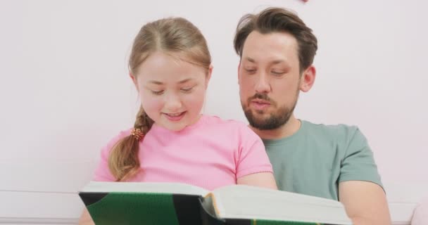 Närbild av far, sitter på soffan, och skrattar tonåring dotter, sitter i hans knä, och tittar på fotoalbumet — Stockvideo