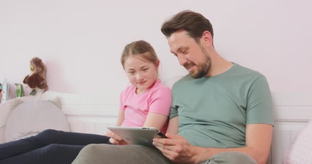 Otec a dospívající dcera sedí na gauči v obýváku, prohlížejí si internetový obchod, užívají si víkend Dívka jí chce něco koupit, ale její otec s tím nesouhlasí. — Stock video