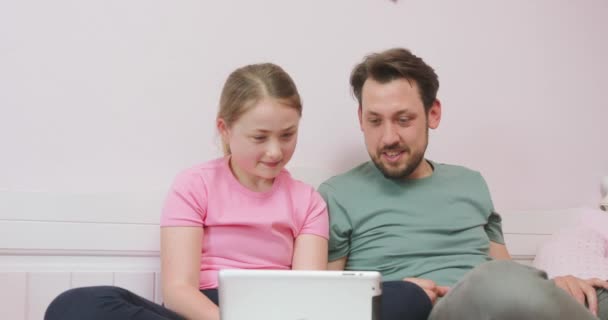 Ojciec i nastoletnia córka siedzą na kanapie w salonie, oglądając futbol online, ciesząc się weekendem Ojciec i córka wspierają swoją drużynę piłkarską, trzymają kciuki i są — Wideo stockowe