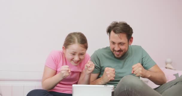 父と10代の娘は、リビングルームでソファに座って、サッカーをオンラインで見て、週末を楽しんでいます父と娘は彼らのサッカーチームをサポートし、指を交差させ、 — ストック動画