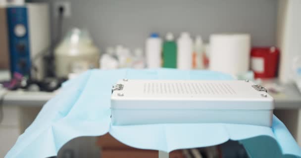 Tutup meja dengan wadah sterilisasi dengan alat steril, di mana dokter hewan laki-laki mengenakan wadah sterilisasi lain Di latar belakang dinding kabur dan meja dengan medis — Stok Video