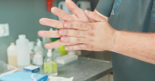 Feche as mãos do veterinário masculino, enquanto ele esfrega as mãos juntas espalhando um desinfetante antes de uma operação No fundo parede borrada e uma mesa com recipientes poliméricos médicos — Vídeo de Stock