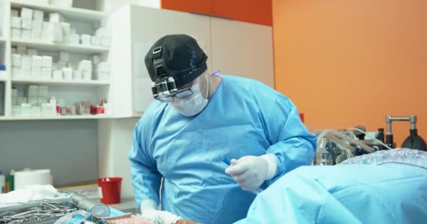 Homme vétérinaire, en tenue chirurgicale, prépare des outils chirurgicaux et électroniques pour commencer la chirurgie sur le chien En arrière-plan - murs orange et armoires blanches avec des médicaments — Video