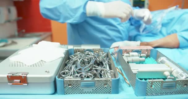 Κοντινό πλάνο του τραπεζιού με δοχεία αποστείρωσης με αποστειρωμένα εργαλεία Δεύτερο πλάνο ελαφρώς θολή - αρσενικό κτηνίατρο σε χειρουργική στολή, προετοιμάζει χειρουργικά και ηλεκτρονικά εργαλεία για να ξεκινήσει η χειρουργική επέμβαση σε — Αρχείο Βίντεο