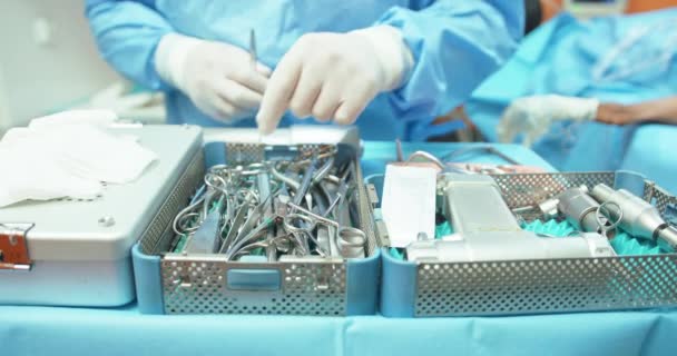 Närbild av bord med sterilisering behållare med steriliserade verktyg Andra planen något suddig - manlig veterinär i kirurgisk outfit, förbereder kirurgiska och elektroniska verktyg för att starta kirurgi på — Stockvideo