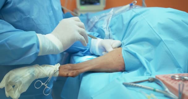 Primer plano de las manos de un veterinario masculino, con guantes blancos, y en traje quirúrgico, mientras hace una incisión en la pierna posterior de un perro anestesiado durante la cirugía — Vídeos de Stock