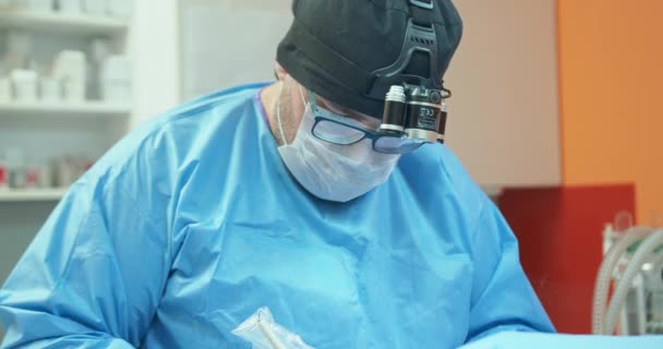 Homme vétérinaire, dans des lunettes, gants blancs, casquette et en tenue chirurgicale, alors qu'il opère la jambe arrière d'un chien anesthésié pendant la chirurgie En arrière-plan - murs orange, armoires blanches avec — Video