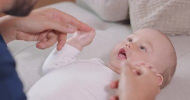 Bebeğin kanepede sırtüstü yatıp bebeğin yanında diz çöken babasına bakarken onunla oynar, gülümser ve konuşur.