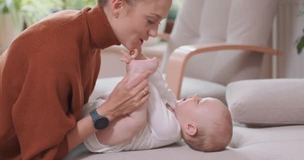 Bebeğin sırtını kanepeye yaslayıp gülümseyerek ve mutlu bir şekilde ayaklanıp, bebeğin yanında diz çöken annesine bakarak gülümseyerek sandalyesini ve penceresini öpüyor. — Stok video