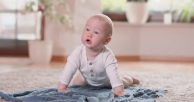 Küçük bebeğin halıda, battaniyenin üzerinde emeklemesini, arka plandaki dört beyaz duvarın, pencerenin ve yeşil bitkilerin üstünde yükselmesini.